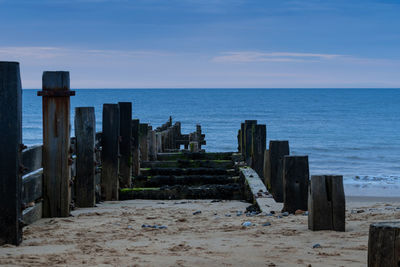 Wooden posts on beach against sky