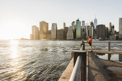 Usa, brooklyn, man doing stretching exercises in front of manhattan skyline in the evening