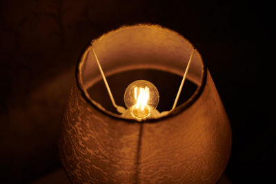 Incandescent light bulb in round lampshade glowing in dark. extremely dusty lamp, lit light bulb