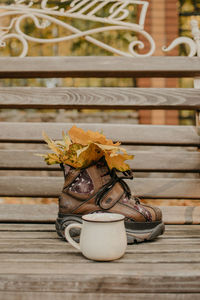 Hello fall, autumn season, fall mood. yellow maple leaves in boot and enamel cup on bench in fall