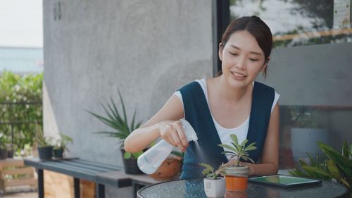 Young woman looking at potted plant on table