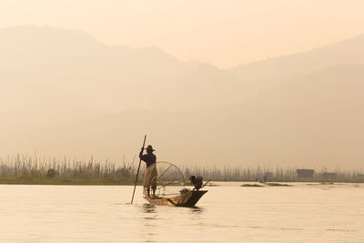 Man on boat against sky during sunset