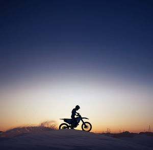 Silhouette man riding bicycle against orange sky