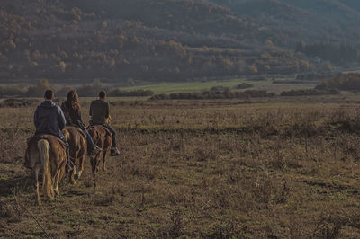 Rear view of people riding horse on field