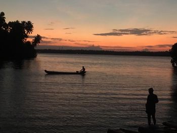 Silhouette people in sea against sky during sunset