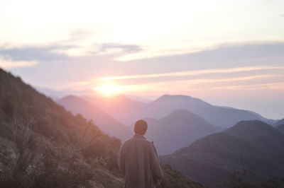 Rear view of man looking at mountains against sky during sunset