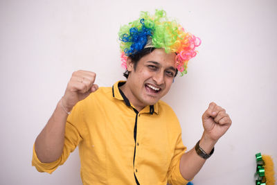 Portrait of cheerful man wearing colorful wig standing against wall