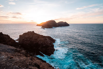 Rocks in sea against sky during sunset