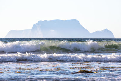 Waves rushing towards sea shore against mountain