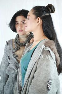 Portrait of young woman with friend standing against wall at home