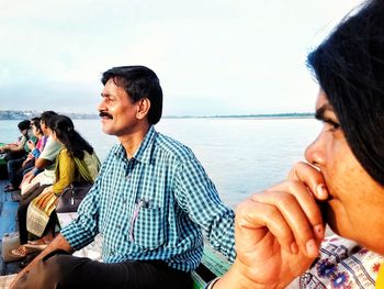Man and woman sitting on sea shore against sky