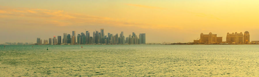 Sea and buildings against sky during sunset