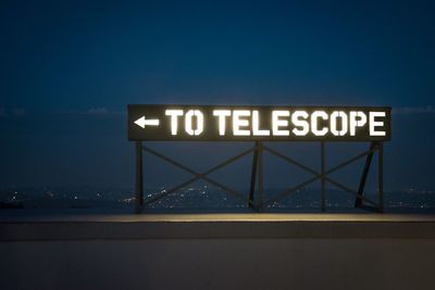 Information sign against clear blue sky at night