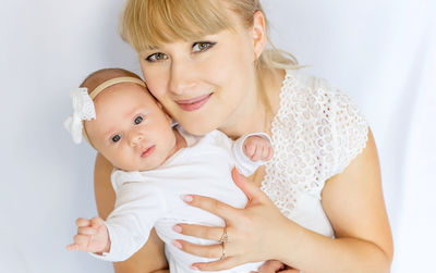 Portrait of smiling woman holding baby in hand against white background