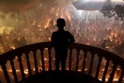 Rear view of silhouette man standing by illuminated railing in city