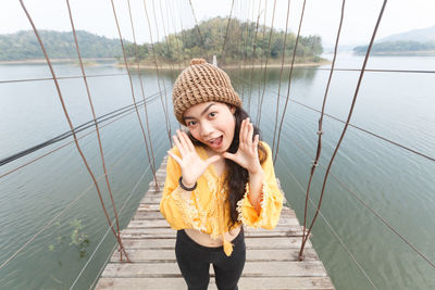 Portrait of young woman standing on footbridge over lake