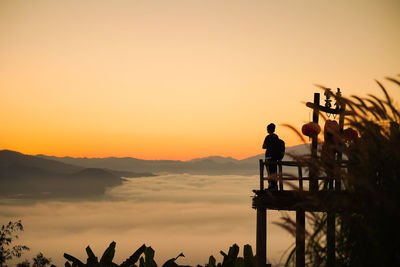 Silhouette people standing on mountain against orange sky