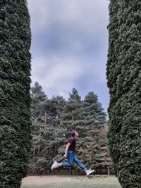 Side view of man jumping by trees against sky