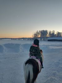 Rear view of person riding horse on snow covered land