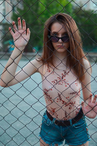 Portrait of young woman standing against chainlink fence