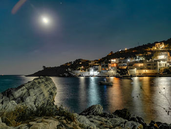 Sea by illuminated buildings against sky at night