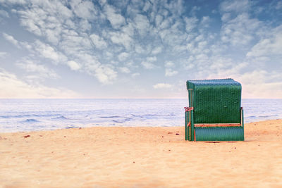 A green wicker beach chair stands in the sand on the ocean and enjoys the romantic view over the sea