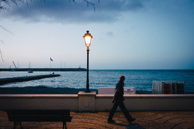 Woman walking on street by sea against sky