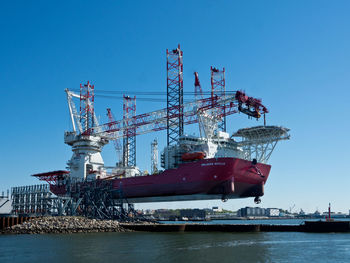 Cranes at commercial dock against clear blue sky