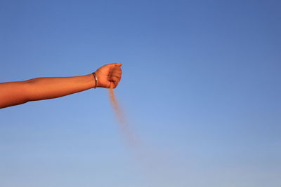 Low angle view of cropped hand releasing sand against sky