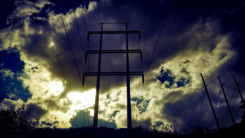 Low angle view of silhouette electricity pylon against cloudy sky