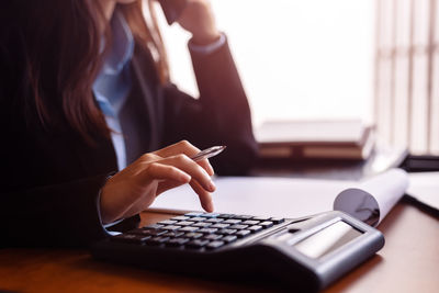 Midsection of businesswoman using calculator on desk in office