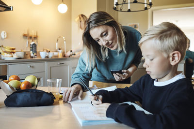 Mother assisting son while doing homework at home