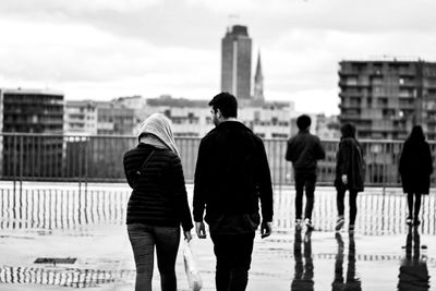 Rear view of people walking in city against sky