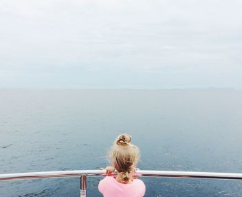 Rear view of girl standing by railing at sea against sky
