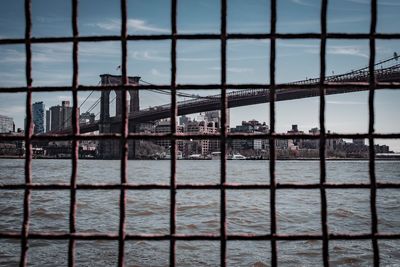 Brooklyn bridge over river with buildings in city against sky