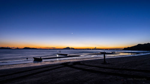 Scenic view of beach against clear sky at sunset