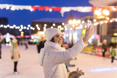 Midsection of woman standing against illuminated city at night