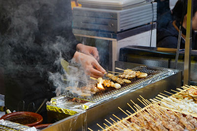 Person preparing food on barbecue grill at market