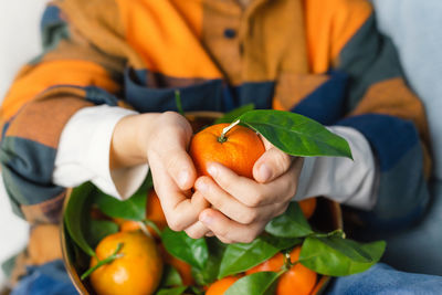 Close view of the hands of a child holding a tangerine. bright colors.