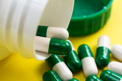 Close-up of pills spilling from bottle on yellow background