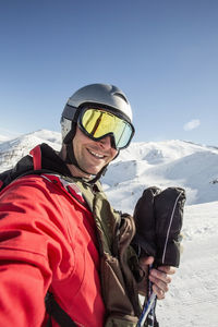 Smiling man in ski-wear standing on snow covered field against clear sky