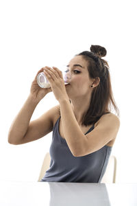 Portrait of a young woman drinking glass against white background