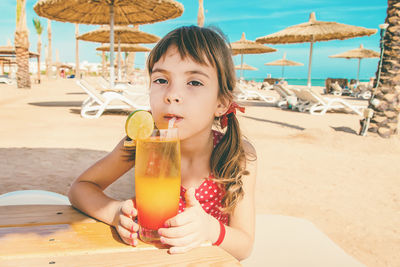 Portrait of young woman holding drink at beach