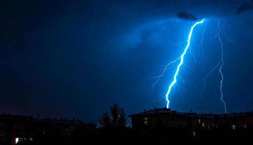 Low angle view of lightning over houses at night