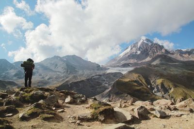 Rear view of man standing on mountain against cloudy sky