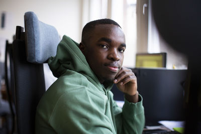 Side view portrait of male trainee in green hooded shirt sitting at office