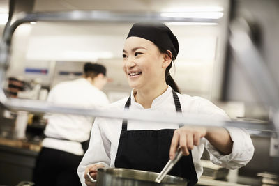 Smiling female chef stirring pot in kitchen at restaurant