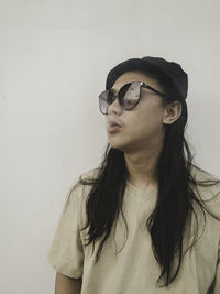 Young woman wearing sunglasses against wall