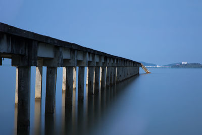 Wooden posts in lake against clear blue sky