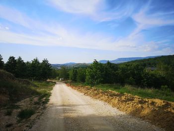 Dirt road amidst plants and trees against sky